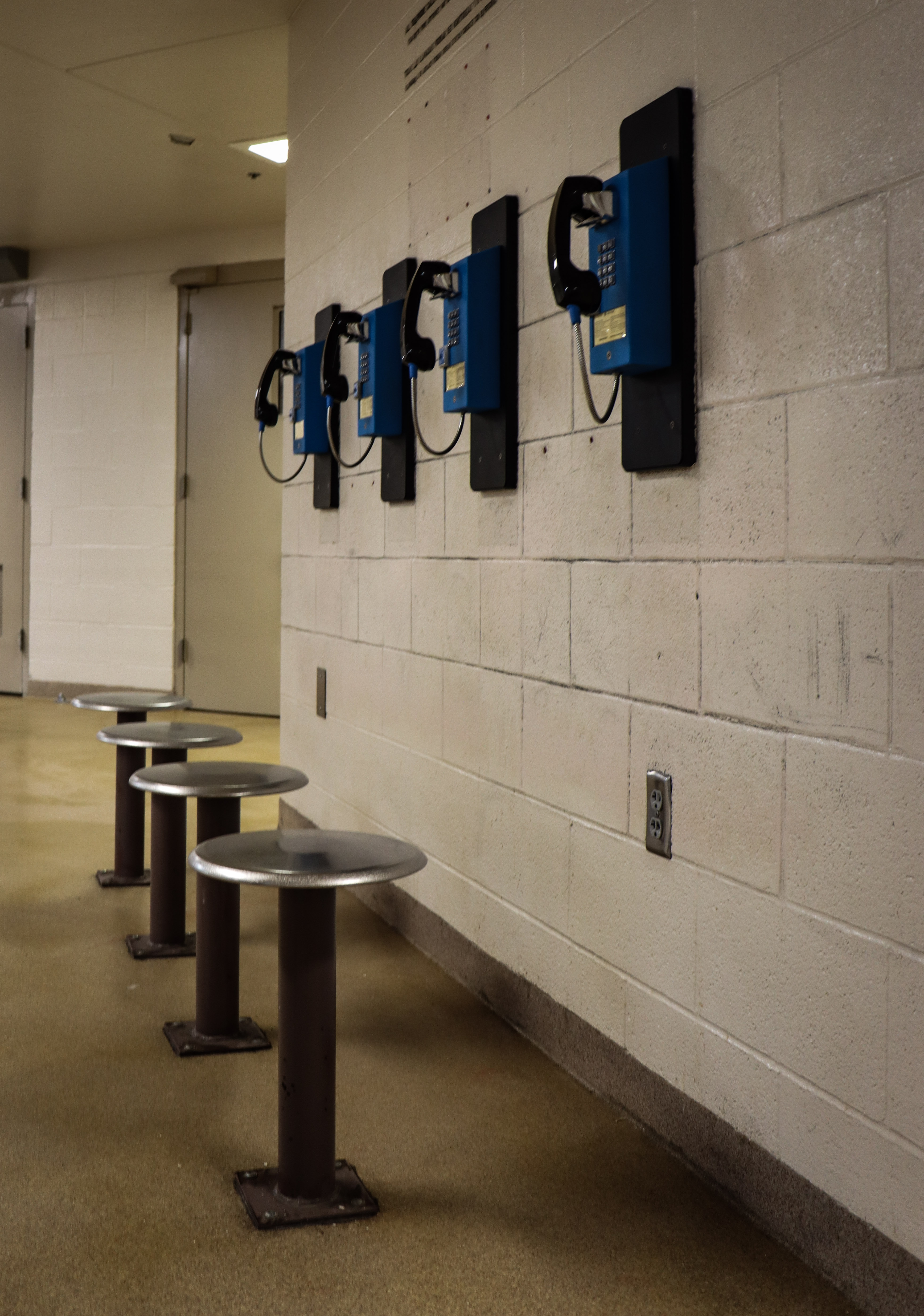 Telephones and stools lined in a row in a jail facility for inmates to use.